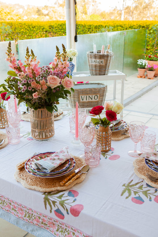 Decorative outdoor table setting with flowers, plates, and glasses on a floral tablecloth.
