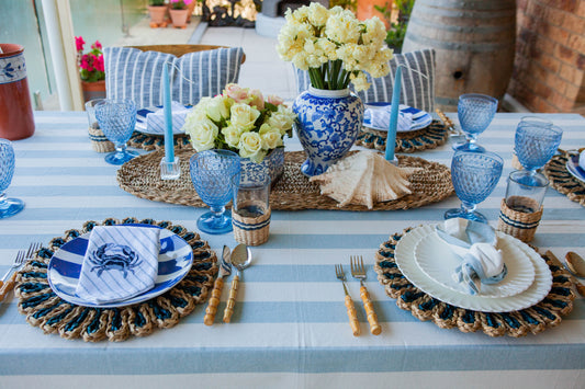 Elegant outdoor table setting with blue and white decor, flowers, and striped tablecloth.