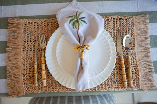 Table setting with white plates, palm embroidered napkin, and cutlery on textured placemat