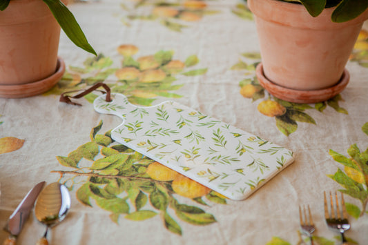 Table setting with a decorative card on a floral tablecloth, potted plants, and cutlery.