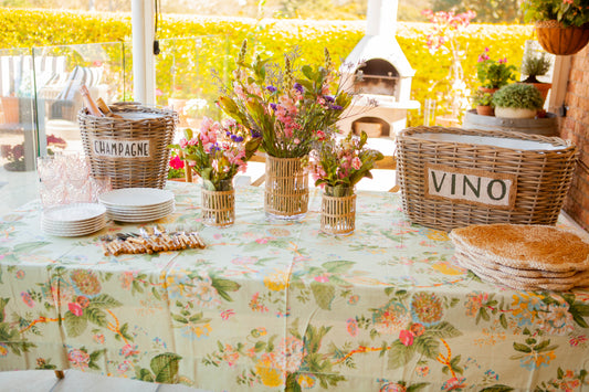 Decorated table with floral tablecloth, baskets labeled 'Champagne' and 'Vino', and potted plants.