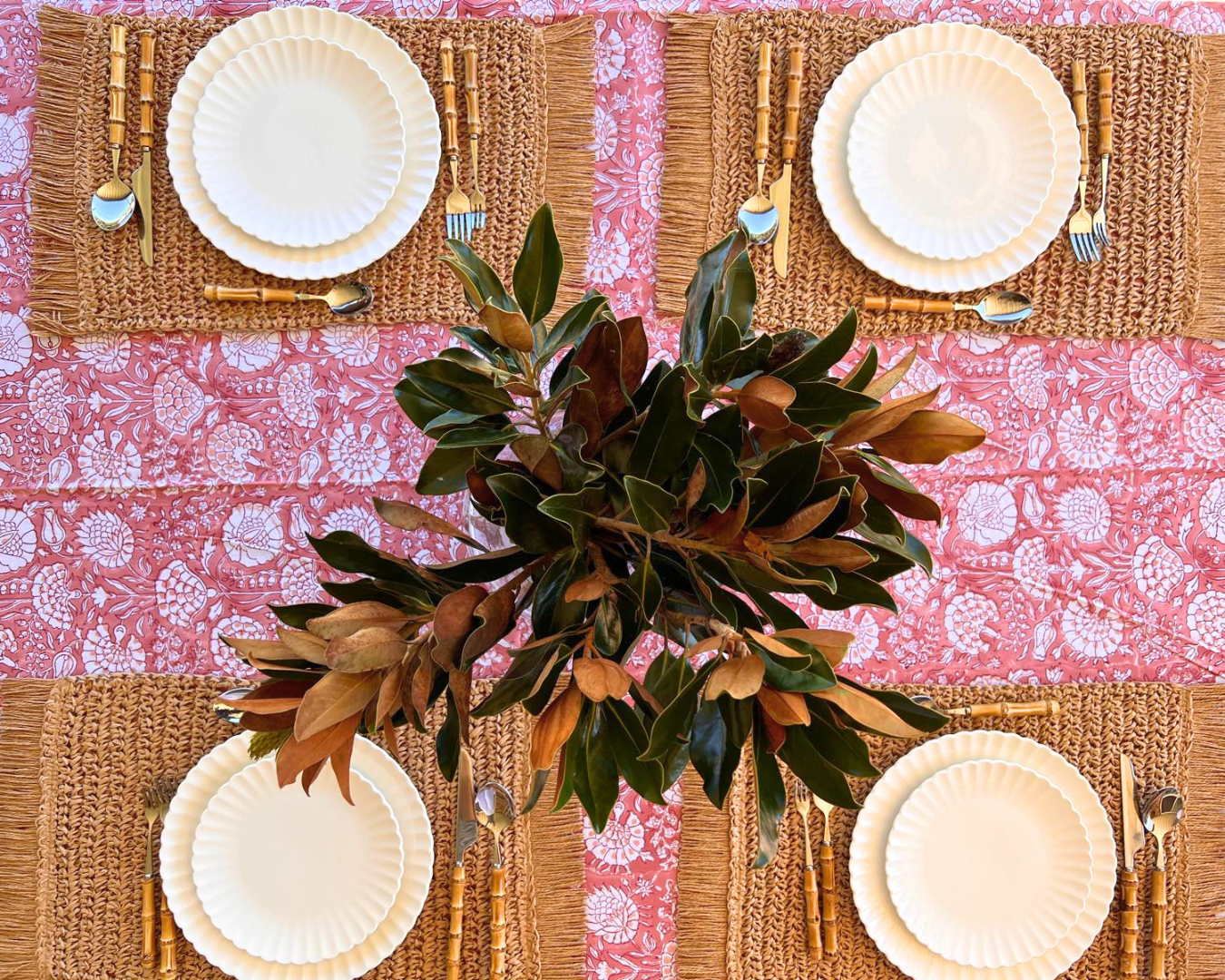 Table setting with woven placemats, white plates, and a pink floral tablecloth.
