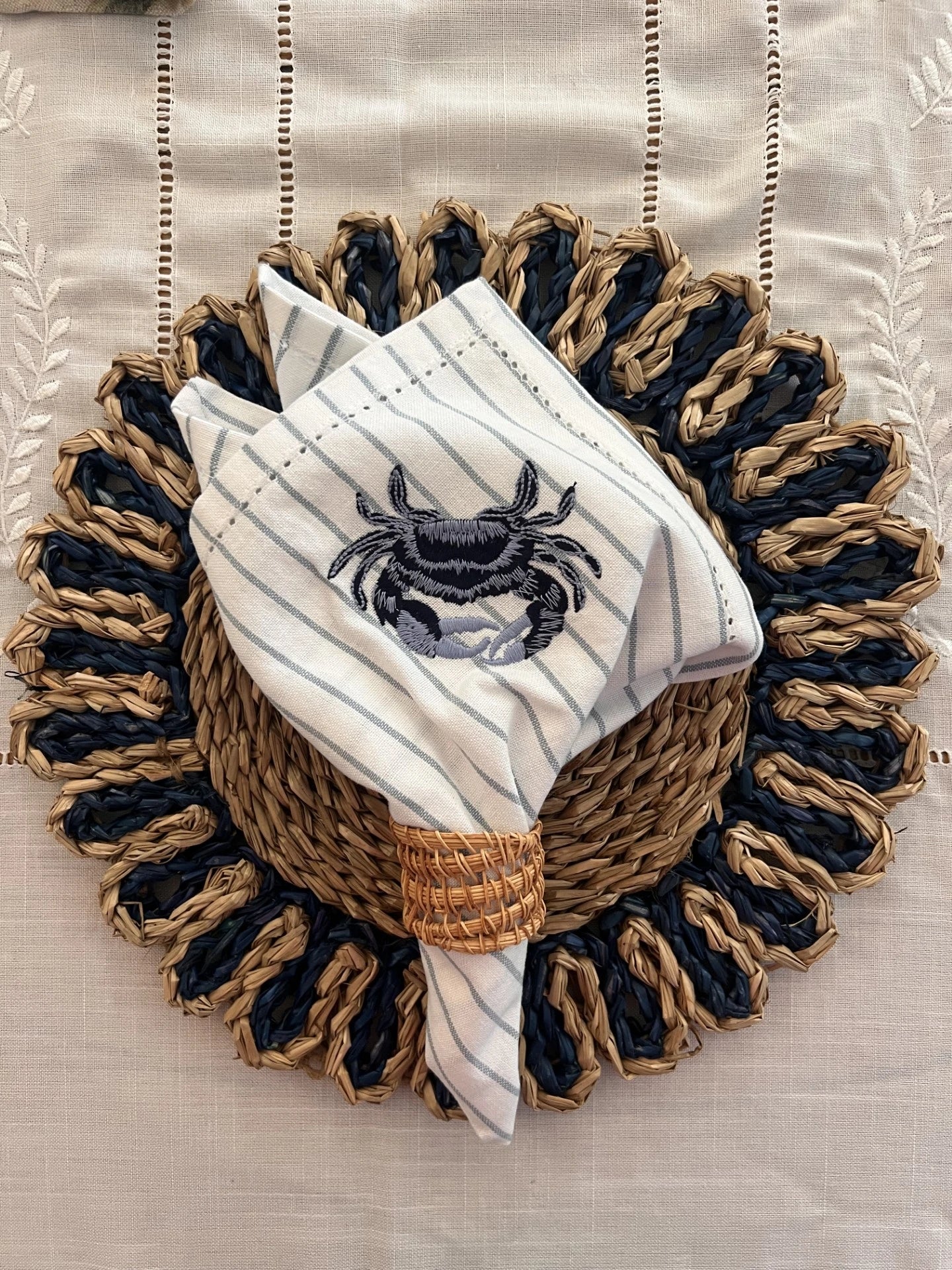 Stripe cotton napkin with crab embroidery on top of navy dual woven placemat