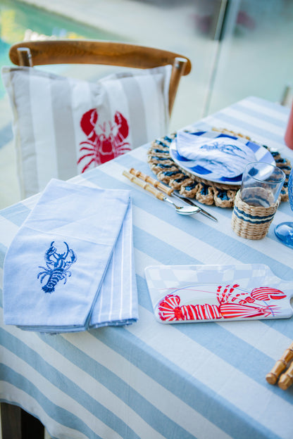 Table setting with lobster-themed napkins and placemats on a striped tablecloth.