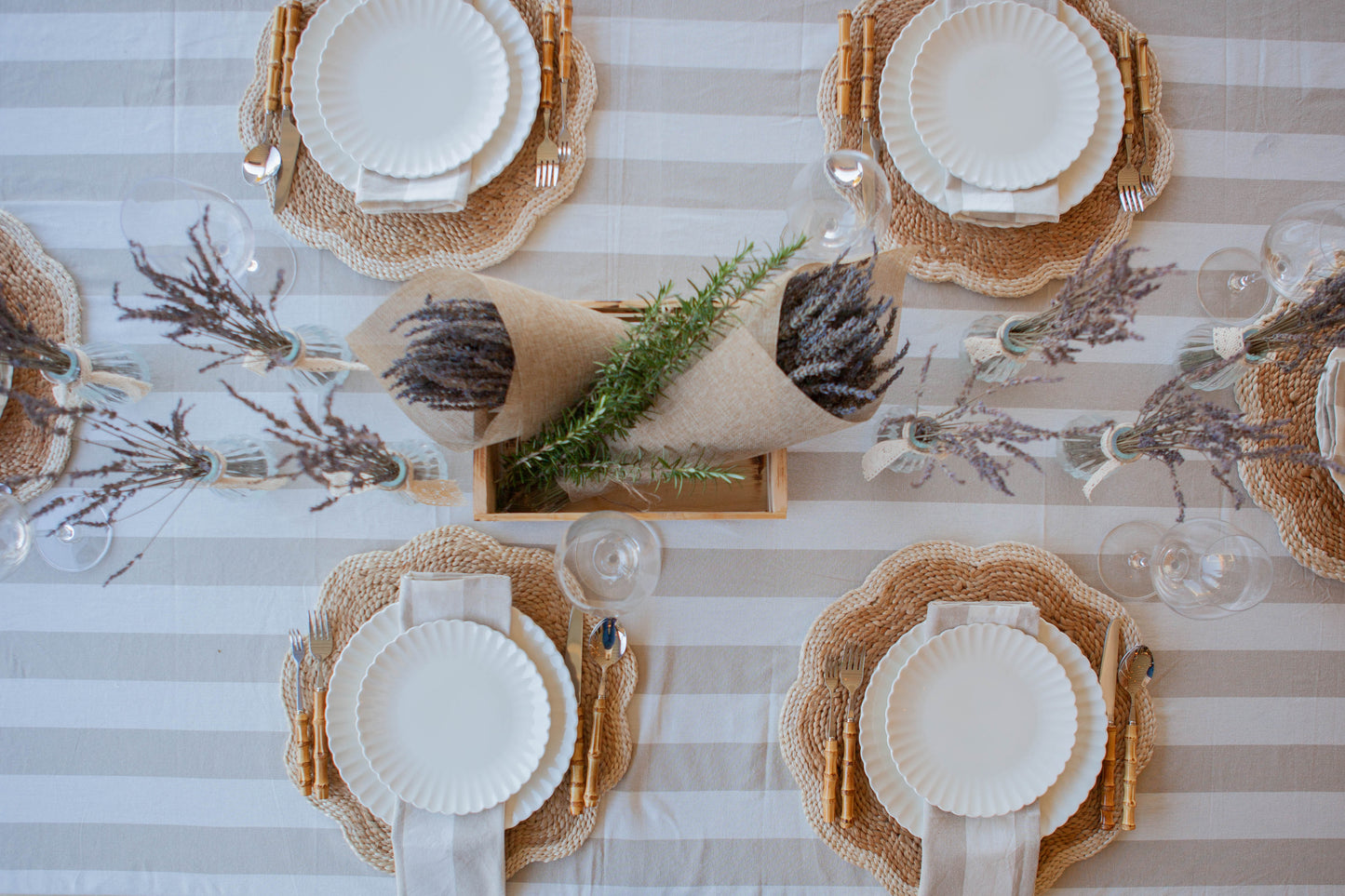 Top-down view of a table setting with white plates, woven placemats, and decorative elements on a striped tablecloth.