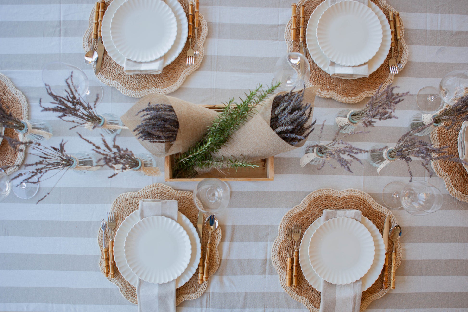 Top-down view of a table setting with white plates, woven placemats, and decorative elements on a striped tablecloth.