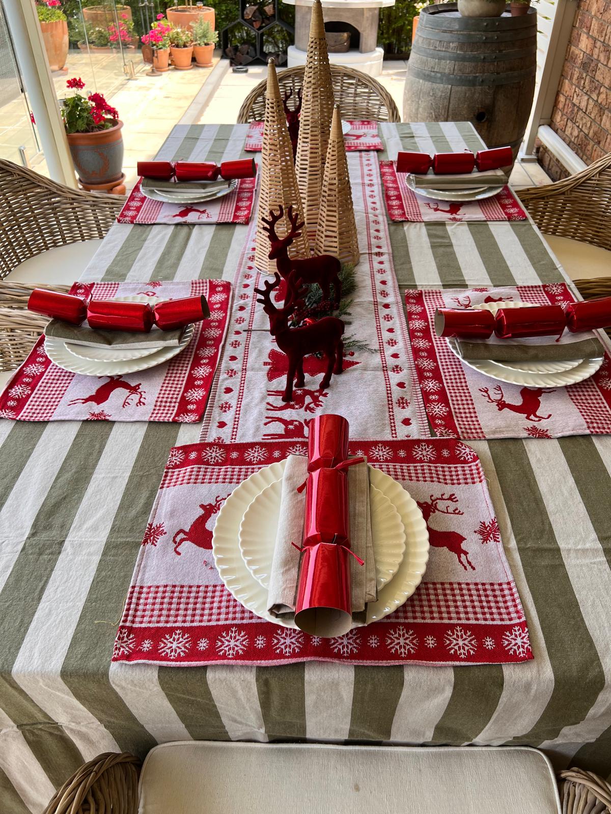 Christmas-themed table setting with striped tablecloth, reindeer, and crackers.