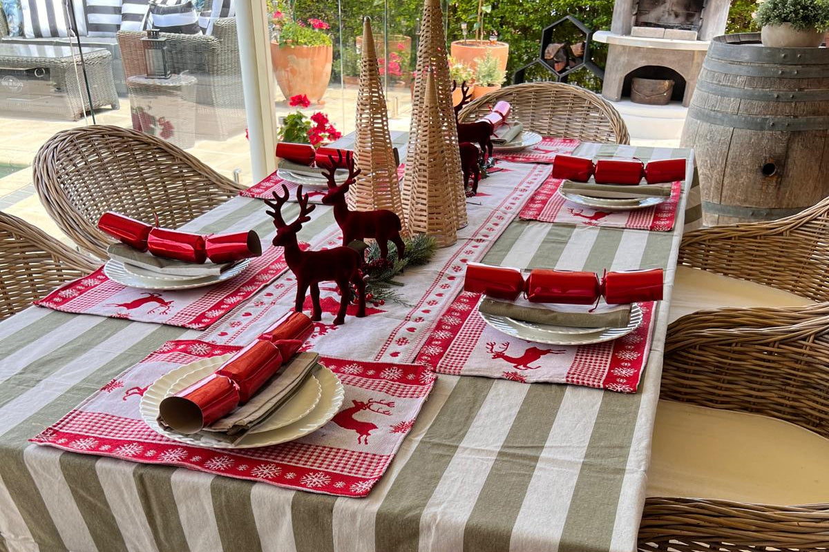 Dining table set for Christmas with striped tablecloth, red placemats, and decorative items outdoors.