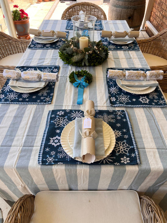 Decorative table setting with blue and white striped tablecloth, snowflake placemats, and Christmas decorations.